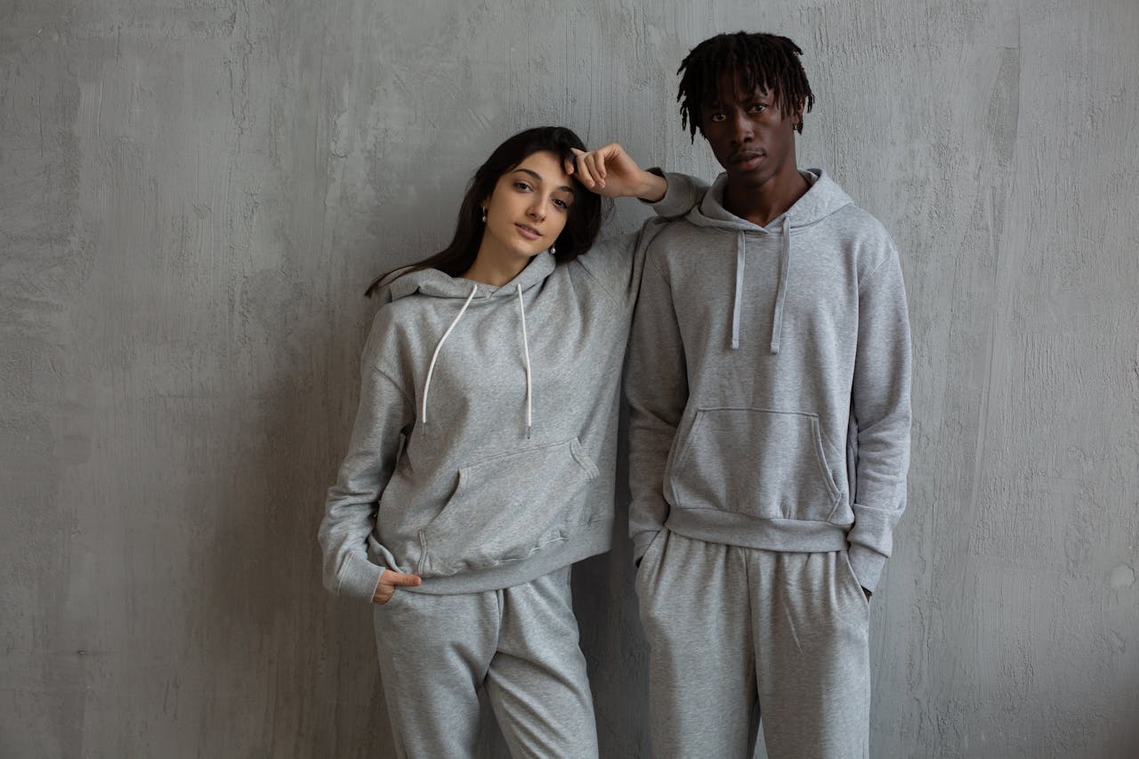 Young multiracial sportspeople wearing gray comfy hoodies and pants standing with hands in pockets and looking at camera